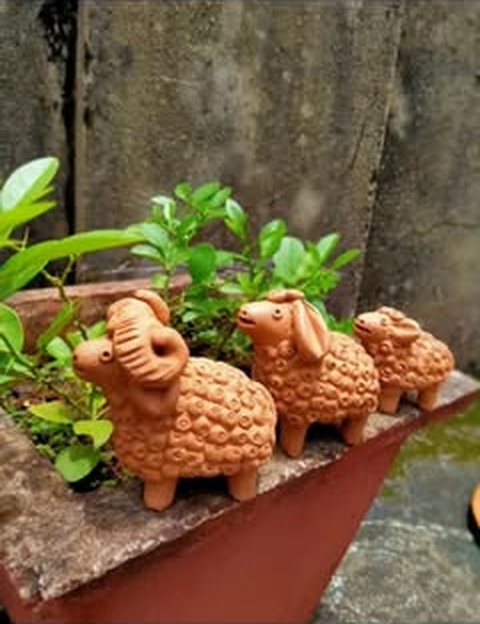 Three handmade terracotta sheep on a planter ledge